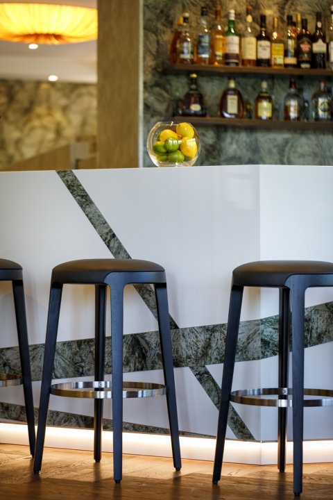 Schwarze Barstühle vor einer Bar mit HPL-Wänden in einem organischen, grünen Muster durchbrochen mit geometrischen, weissen Platten.