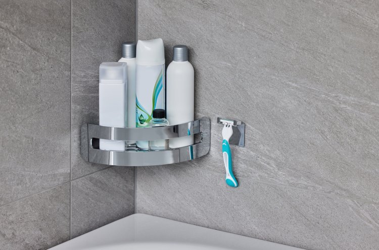 Silberner Korb mit Shampooflaschen in der Ecke einer Badewanne, daneben ein silberner Halter für den Rasierer.