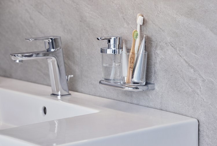 An der Wand befestigtes Zahnputzglas und Seifenspender aus Chromstahl und Glas über einem weissen Waschbecken.