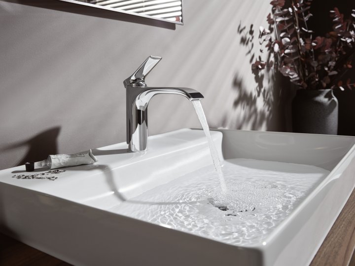 Weisses Keramikwaschbecken das von einer Armatur in glänzendem Chromstahl mit Wasser gefüllt wird.
