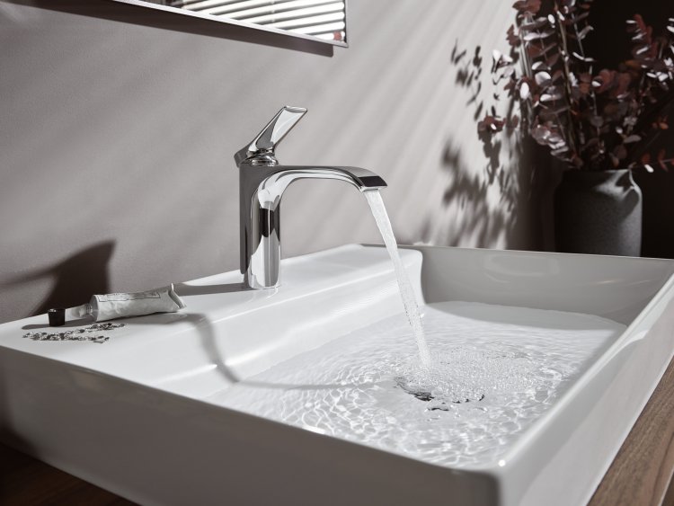Weisses Keramikwaschbecken das von einer Armatur in glänzendem Chromstahl mit Wasser gefüllt wird.