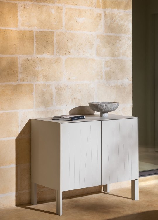 Beiger Aluminiumschrank an einer sonnenbeleuchteten Wand aus gelb-braunem Naturstein im Freien.