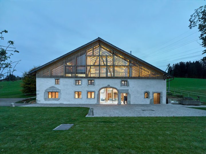 Bauernhaus mit geräumigem, beleuchtetem Dach auf einer Wiese in der Abenddämmerung