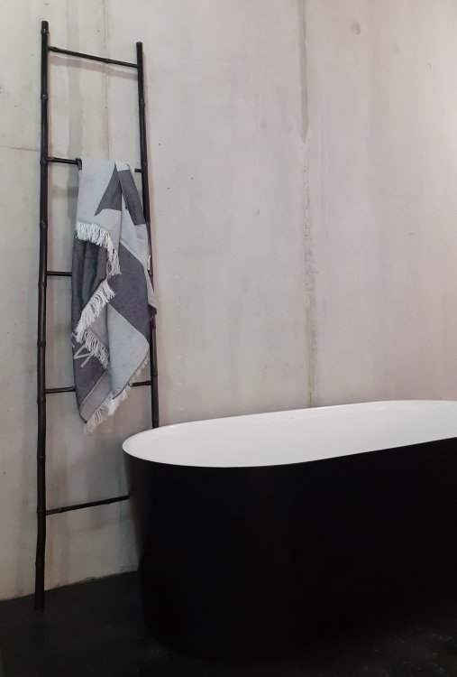 Schwarze Badewanne und schwarze Dekoleiter mit Hamamtuch vor Betonwänden