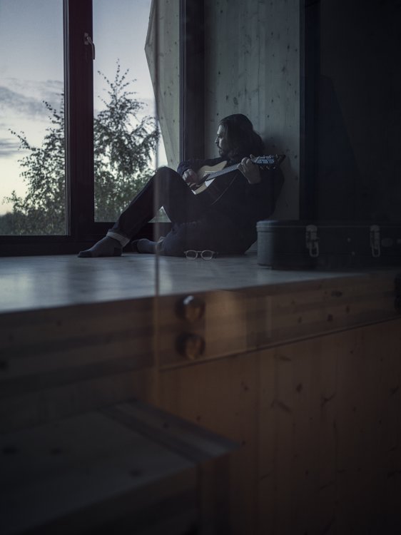 Mann sitzt vor einem Fenster und schaut ins Freie in der Abendstimmung.