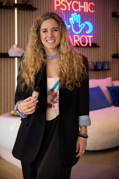 Alessia von Rohr hält ein Räucherbündel und steht vor einem Leuchtschriftzug in Blau und Pink