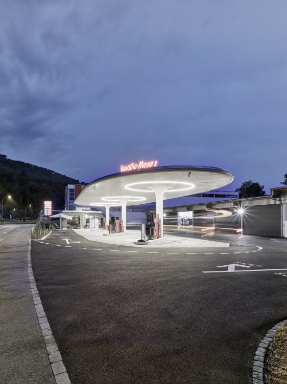 Tankstelle in der nacht mit roter Leuchtanzeige auf dem Dach und beleuchteten Pilzsstützen