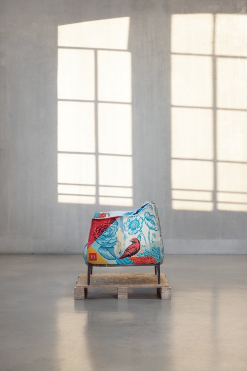 Seitenansicht des farbig bedruckten «Archibald Delicate Balance Limited Edition»-Armchairs auf einer Holzpalette in einem lichten Raum.