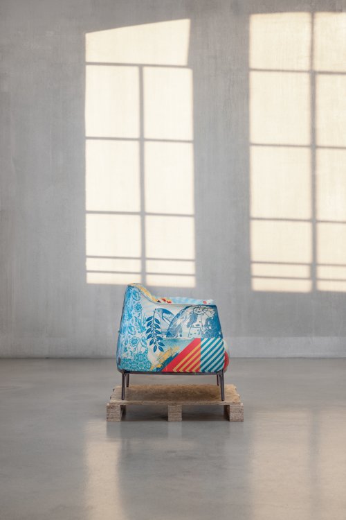 Seitenansicht des farbig bedruckten «Archibald Delicate Balance Limited Edition»-Armchairs auf einer Holzpalette in einem lichten Raum.