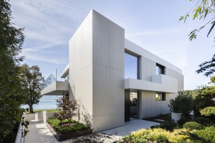 Moderne, kubische Villa am Attersee mit einer hellen Fassade aus Dekton-Paneelen und grosszügigen Glasfronten.