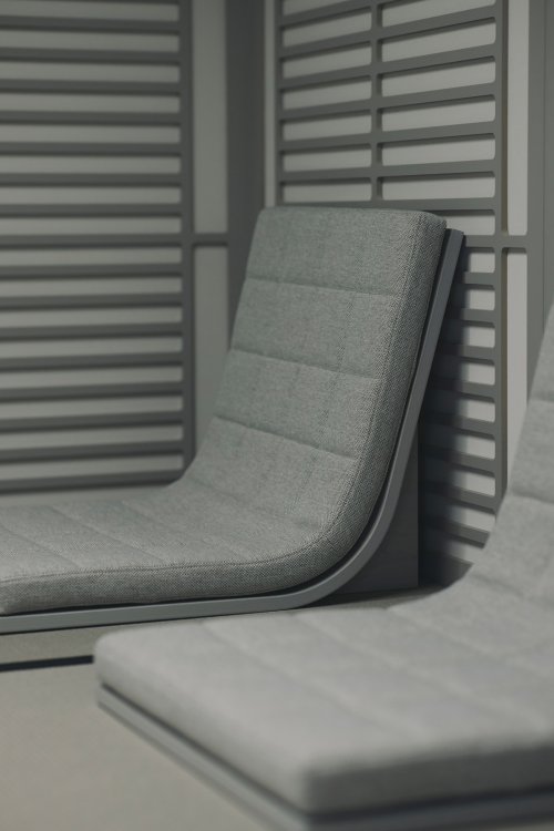 Detailaufnahme eines grau gepolsterten Bodenstuhls mit markanten Quersteppungen im «Sound House». Die Sitzschale aus gebogenem Holz schmiegt sich an eine Wand aus horizontalen Lamellen an, was das minimalistische japanische Design unterstreicht.