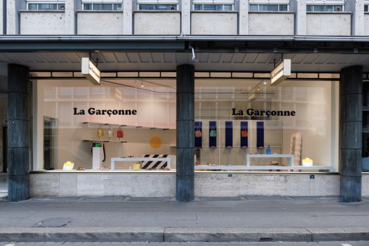 Aussenansicht des «La Garçonne» Stores am Talacker 41 in Zürich. Die grosszügige Schaufensterfront gibt den Blick frei auf das minimalistische Interieur von Naomi Hajnos, geprägt durch weisse Gitterstrukturen, leuchtblaue Akzente und die markante schwarz-weiss gestreifte Verkaufstheke.