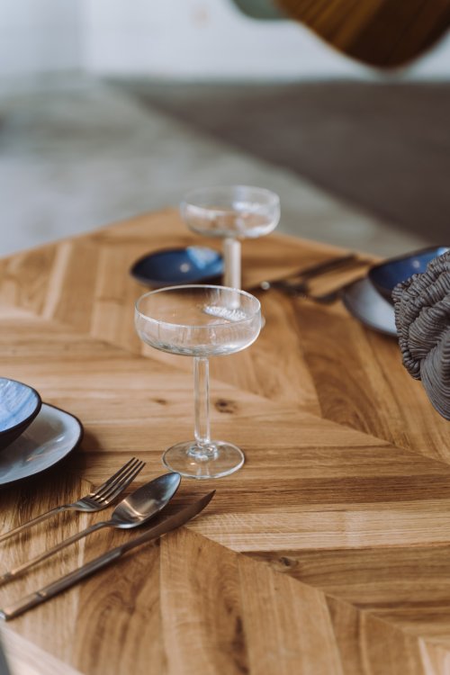 Detailaufnahme eines gedeckten Esstischs aus Fischgrätparkett mit Champagnergläsern, blauem Geschirr und Besteck.