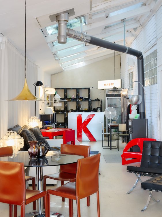 Innenraum des Designgeschäfts Kioskio mit hohen Glasdachfenstern, einer roten Kasse, verschiedenen Designmöbeln und skulpturalen Leuchten.