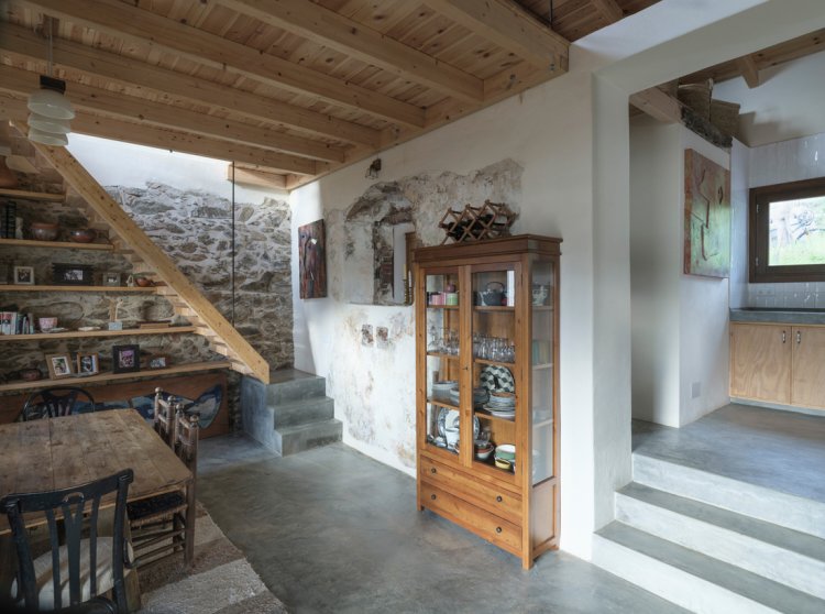 Innenraum von Stone and Water mit freigelegten Steinwänden, Holztreppe, Zementboden und wiederverwendetem Schrank.