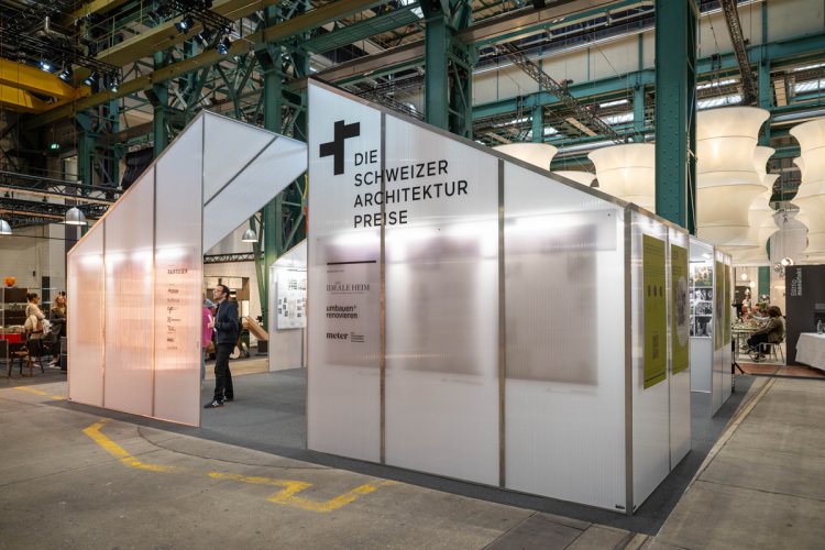 Ausstellungsstand der Schweizer Architekturpreise mit transluzenten Pavillons und grossem Schriftzug in einer Messehalle.
