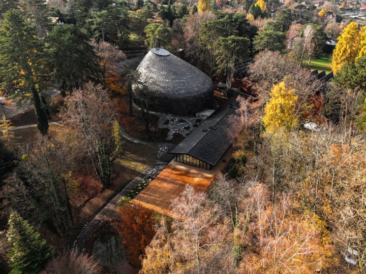 Der kupfergedeckte Saal «La Source Vive» und das verglaste Foyer liegen zwischen Felsen und herbstlich gefärbten Bäumen.