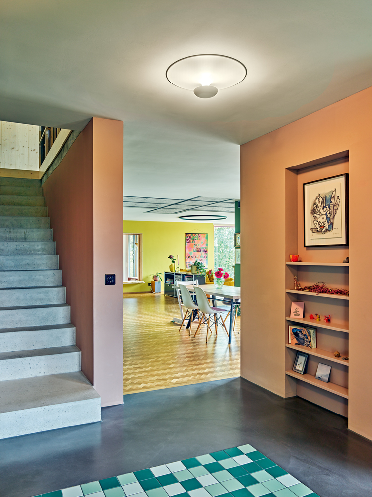 ein Eingangsbereich mit farbigen Wänden, links eine Treppe, am Boden ein Mosaik