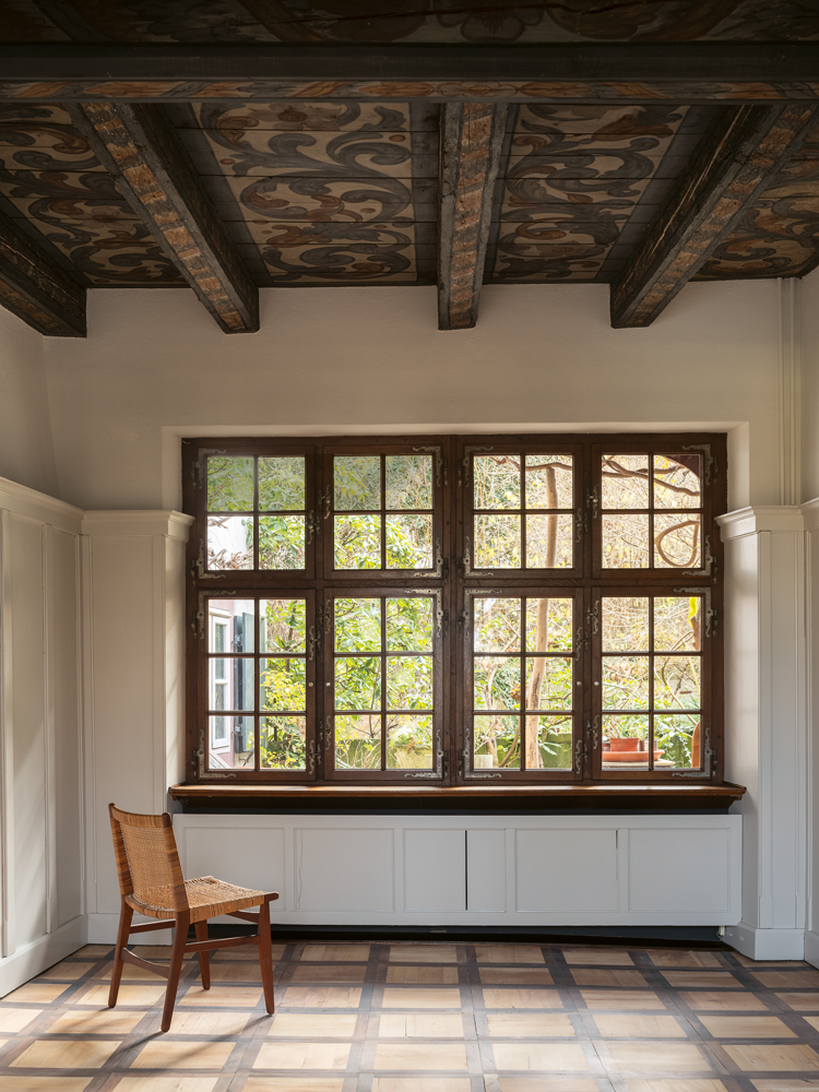 Ein Raum mit einem grossen Fenster, einer alten bemalten Holzdecke und einem Holzboden.
