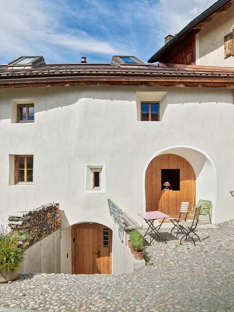 Fassade eines renovierten Engadinerhauses mit einem hölzernen Tor, aus dem ein Hund blick