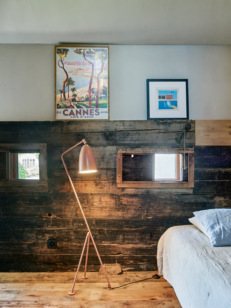 eine alte Holzwand mit kleinen Fenstern, rechts ein Bett