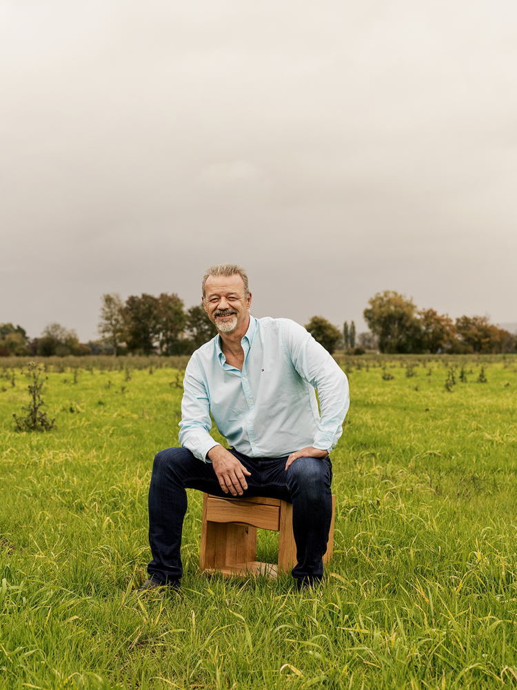 Porträtbild von Adrian Hüsler von Hüsler Nest sitzend auf einem Nachttisch auf einer grünen Wiese.