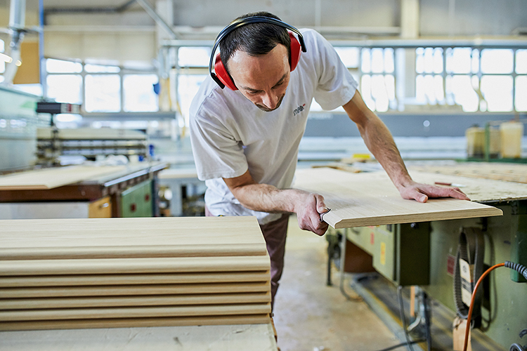 Schreiner der Möbelmanufaktur MAB am Arbeiten an einer Holzsagemaschine.