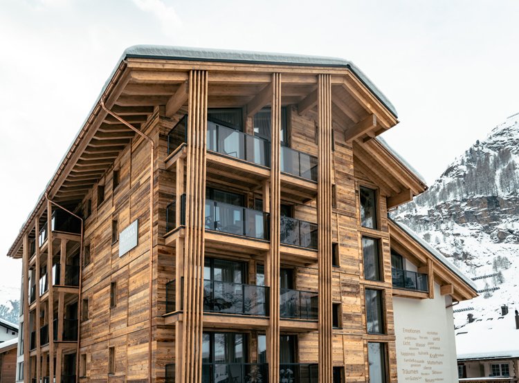 Aussenansicht des Hotels Altiana by La Ginabelle in Zermatt mit einer auffallenden Altholzfassade und Balkonen mit Glasverkleidung.