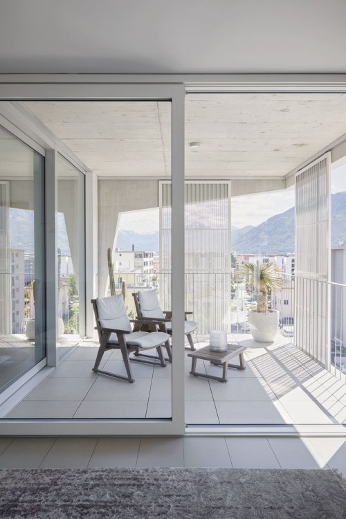 Blick von innen auf den Balkon mit halb geschlossnerer Schiebetüre und Sicht auf die umliegende Landschaft.