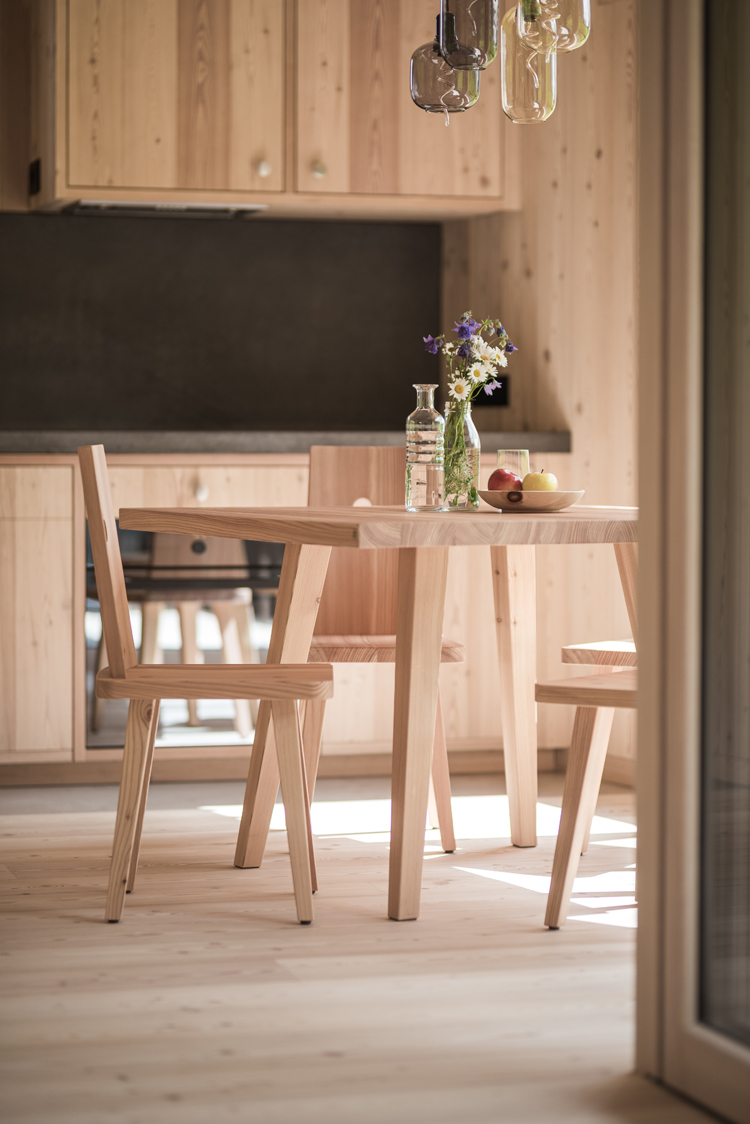 Blick in ein Wohnzimmer verkleidet in heller Lärche mit dunkler Küchenwand sowie Tisch und Stühlen.