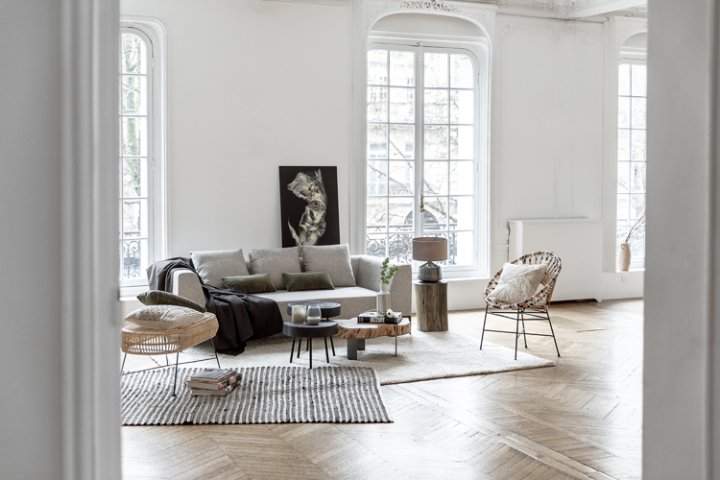 Modernes, helles Wohnzimmer mit drei grossen raumhohen Fenstern und hellem Postersofa, Teppich und einem schwarzen Gemälde an der Wand.