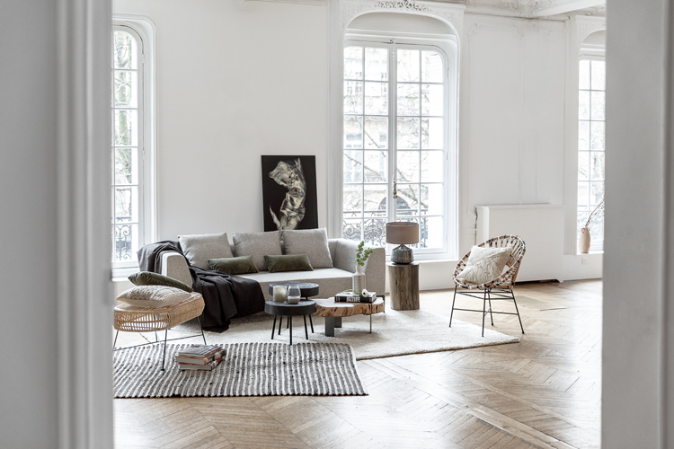 Modernes, helles Wohnzimmer mit drei grossen raumhohen Fenstern und hellem Postersofa, Teppich und einem schwarzen Gemälde an der Wand.