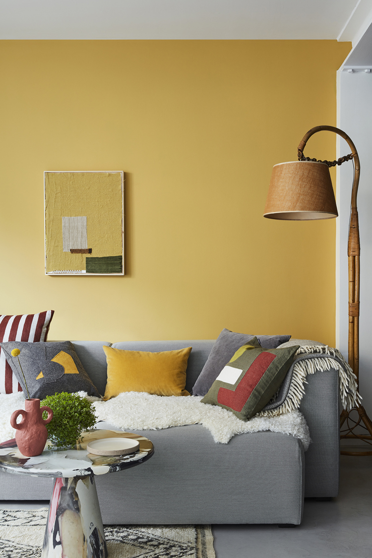 Graues Sofa mit diversen Kissen vor gelber Wand.