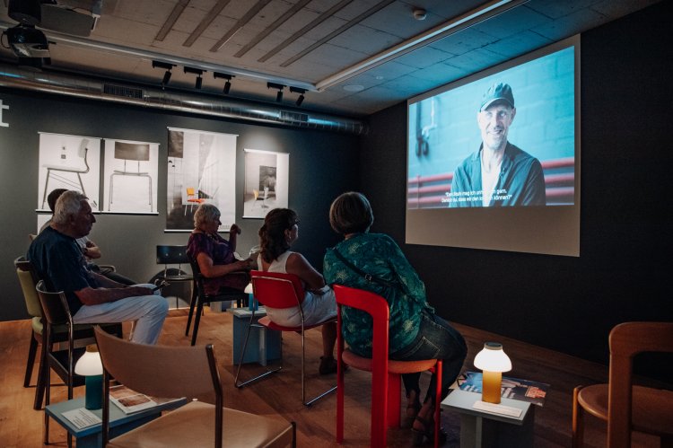 Ausstellung «Das sitzt – 150 Jahre Dietiker Stuhlfabrik» in Stein am Rhein mit Besucher*innen, die einen Film schauen.