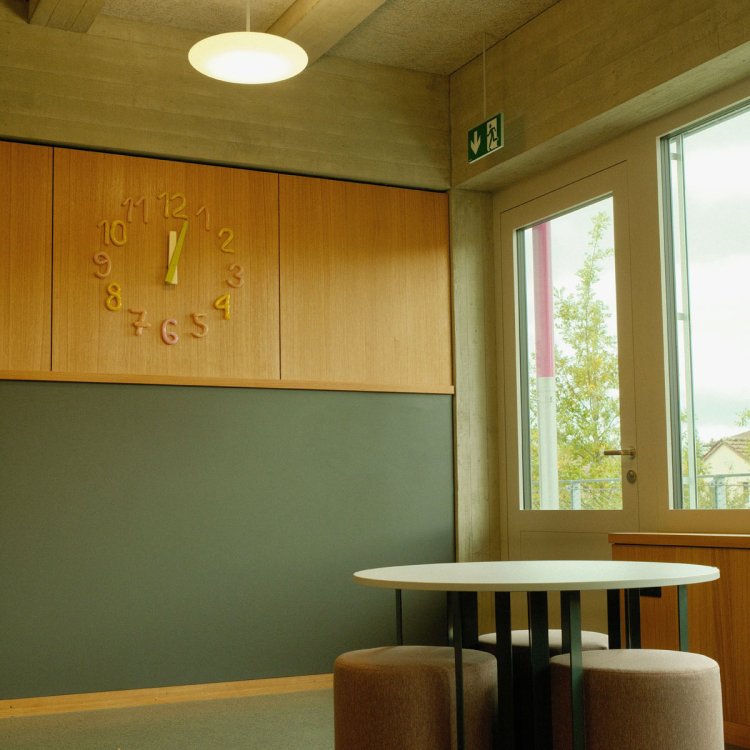 Uhr von ISSU ISSU mit farbcodierten Glasziffern, gestaltet von Cheryl Graf und Mariella Ingrassia, integriert in einen Schulraum.