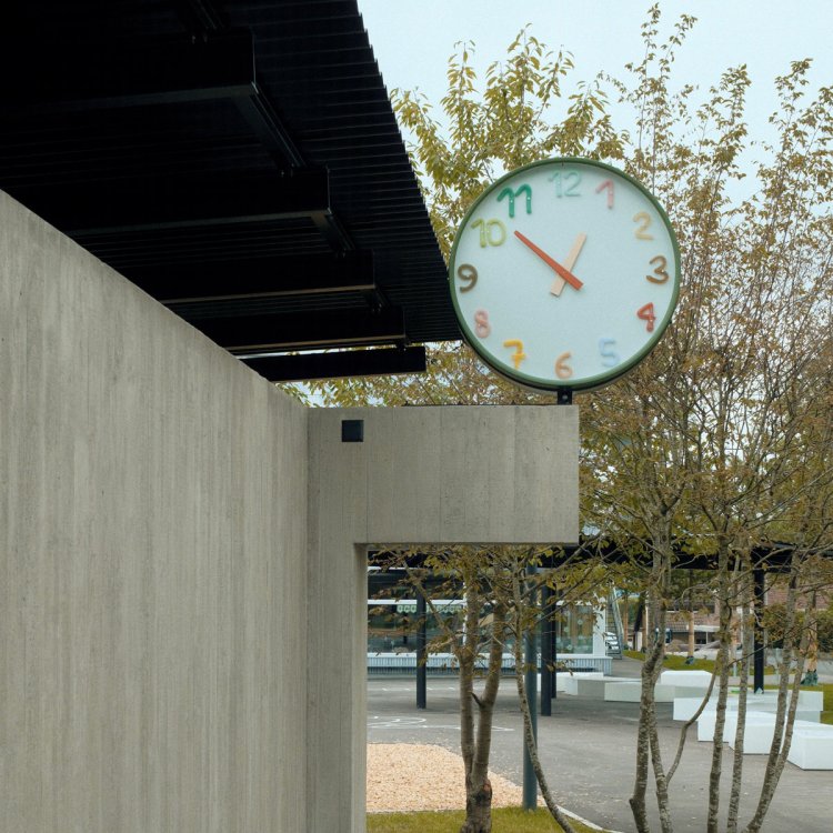 Ausseninstallation der ISSU-ISSU-Uhr mit farbcodierten Glasziffern zur intuitiven Zeitvermittlung im Schulraum.