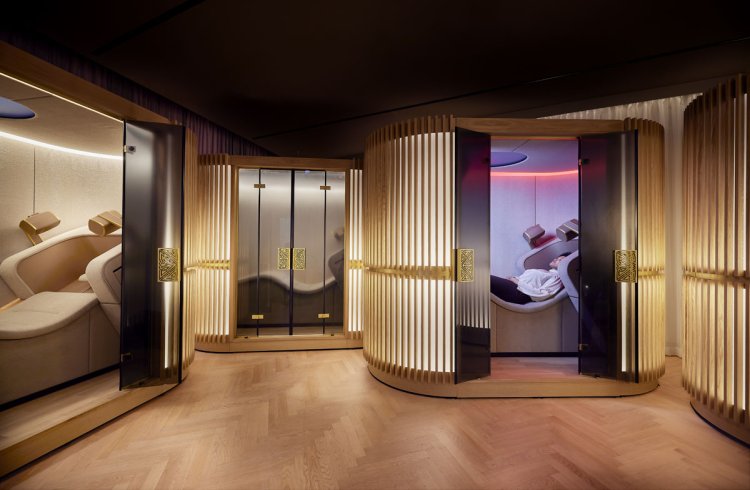 Mehrere beleuchtete Brain-Massage-Pods aus Holz und Glas, in einem davon liegt eine Person entspannt auf einem Liegesessel.