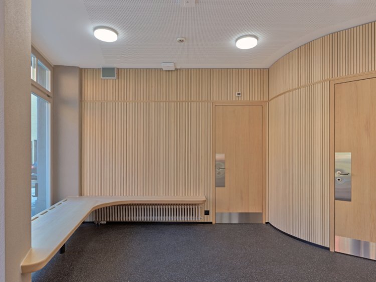 Moderner Aufenthaltsbereich mit Holzvertäfelung, eingebauter Sitzbank, dunklem Bodenbelag und zwei Holztüren.