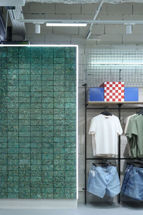 Grün gefärbte Wandfläche aus quadratischen FabBRICK-Ziegeln in einem Ladenraum.