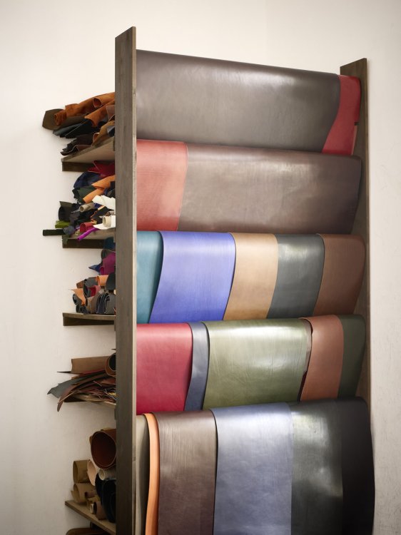 Regal mit aufgerollten Lederhäuten in verschiedenen Farben und Stärken, daneben kleinere Lederreste auf Wandborden.