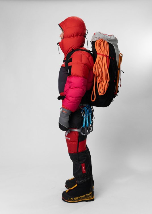 Seitliche Ansicht einer Person in alpiner Expeditionsausrüstung mit Rucksack, Seil und Karabinern.