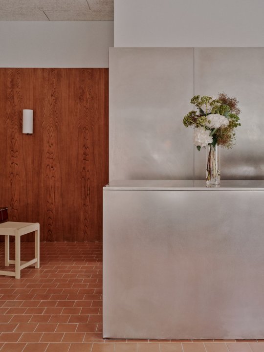 Minimalistisches Café-Interior mit warmen Holzvertäfelungen, Terrakottaboden und reduziertem, modernem Design.