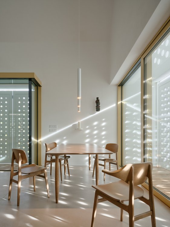 Küche mit Tisch und vier Stühlen. Die perforierten Läden brechen das Licht, das seitlich auf den Tisch fällt.