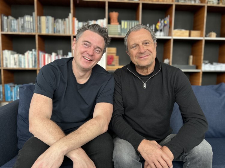 Die beiden Designer Thomas Gardner und Aurel Aebi sitzen nebeneinander auf dem Sofa und lachen in die Kamera.