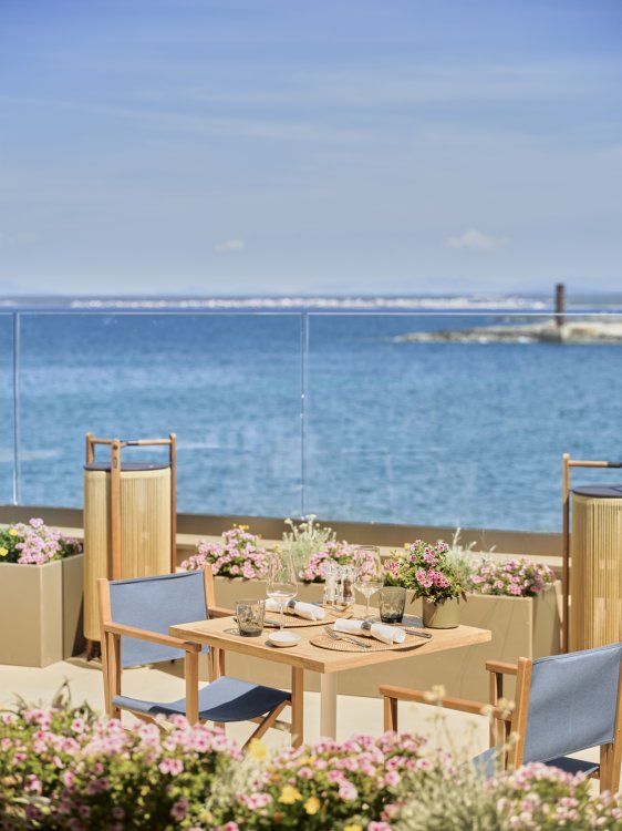 Ein gedeckter Tisch und zwei Stühle auf einer Terrasse mit Blick aufs Meer.