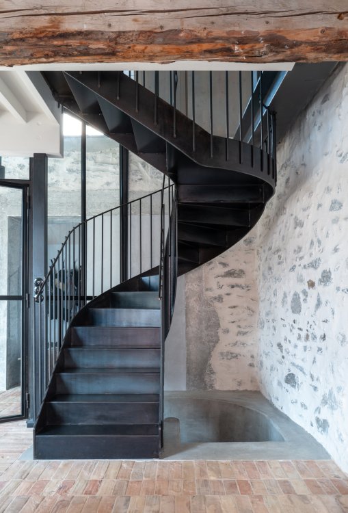 Stählerne Wendeltreppe zwischen hellen Steinmauern und Ziegelboden.