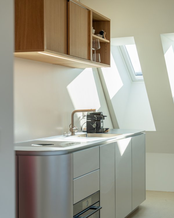 Küchenzeile mit Oberschrank aus Holz und Unterschrank sowie Spüle aus Edelstahl. Die Küche hat abgerundete Ecken.