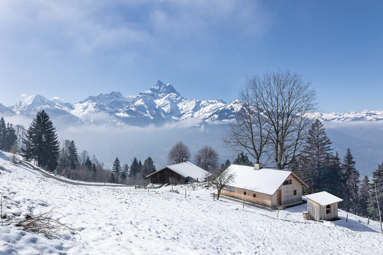 Schlichtes Holzhaus in einer Schnee bedeckten Landschaft mit Blick auf die Walliser Bergewelt.