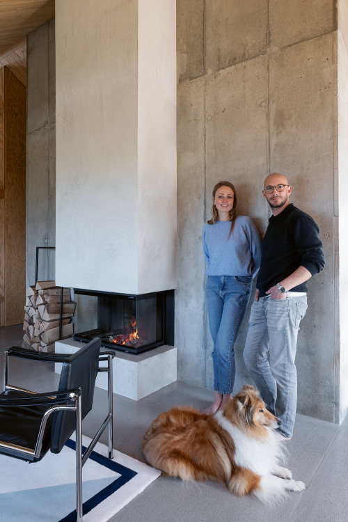 Architekt David Cloux mit seiner Partnerin Johanna und Hund Charlie, ein Kamin im Hintergrund.