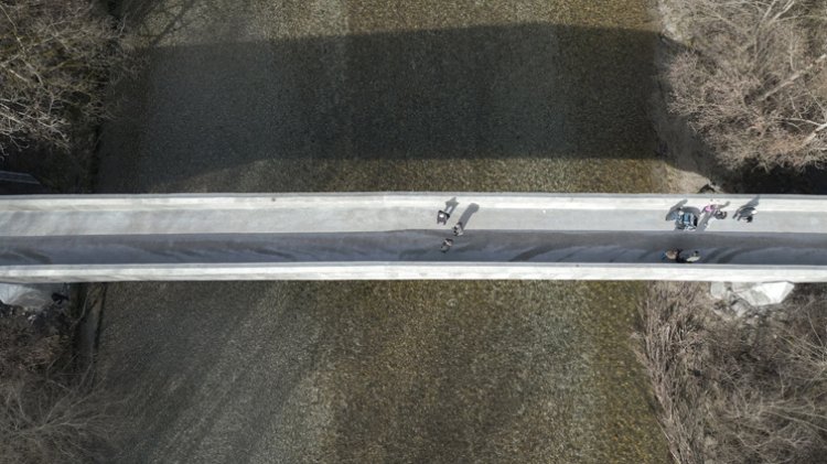 Vogelperspektive auf eine lange schmale Brücke mit einigen Passanten drauf.